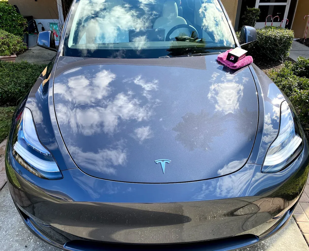 Gray Tesla car, hood reflecting sky, with a wash cloth and detailer on the hood.