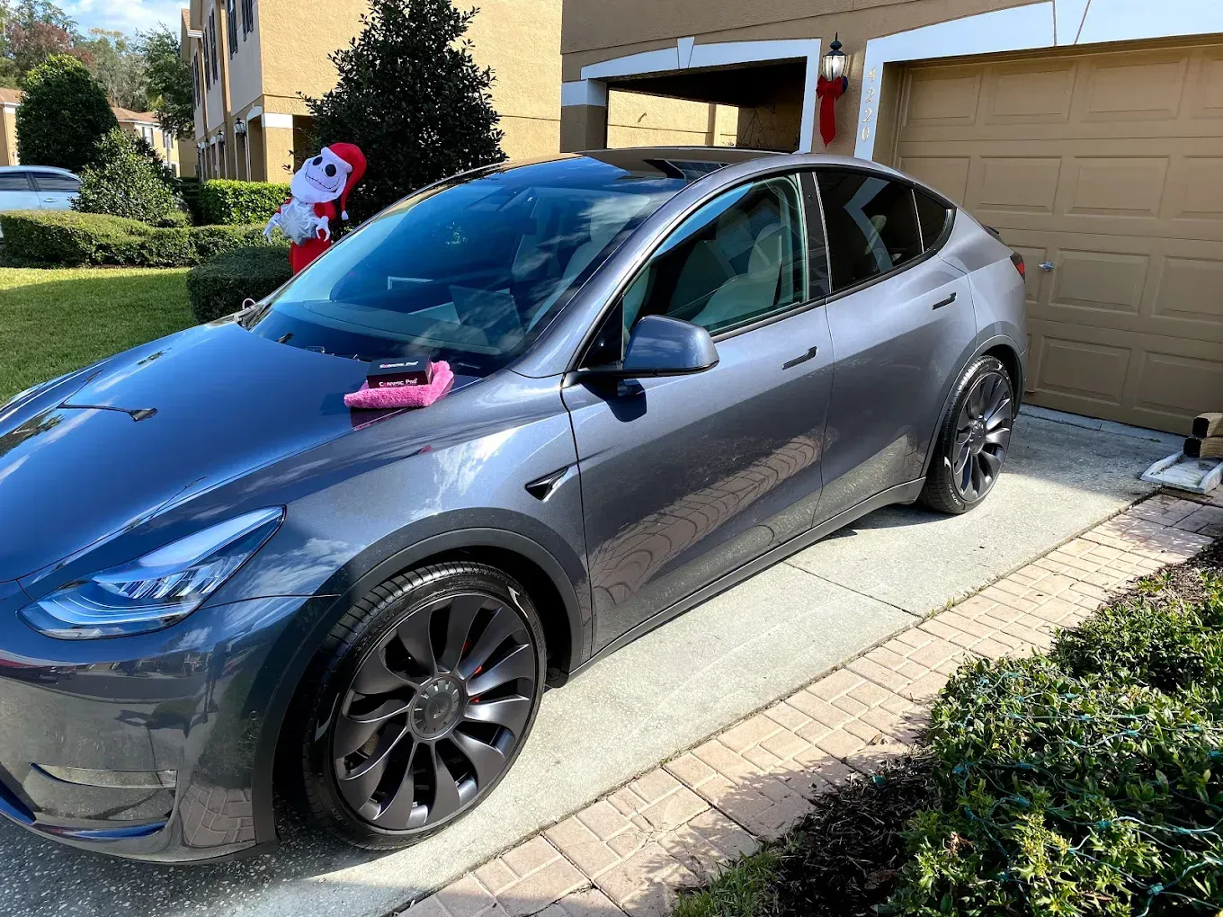 Gray Tesla Model Y parked on a driveway, with a Santa decoration visible nearby.