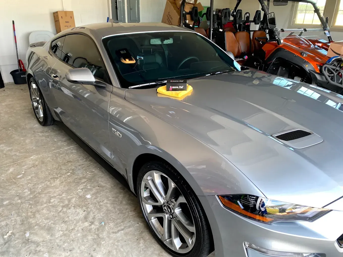 Silver Mustang in a garage, with detailing tools on the hood and golf carts in the background.