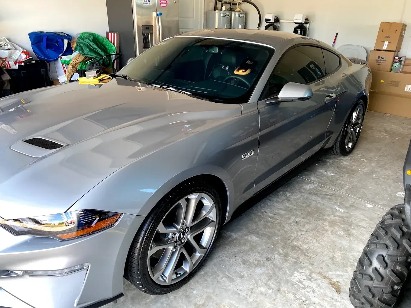 Silver Ford Mustang parked in a garage with tinted windows and chrome rims.
