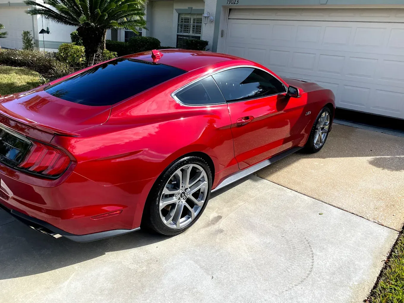 Red Ford Mustang parked in a driveway, next to a garage.