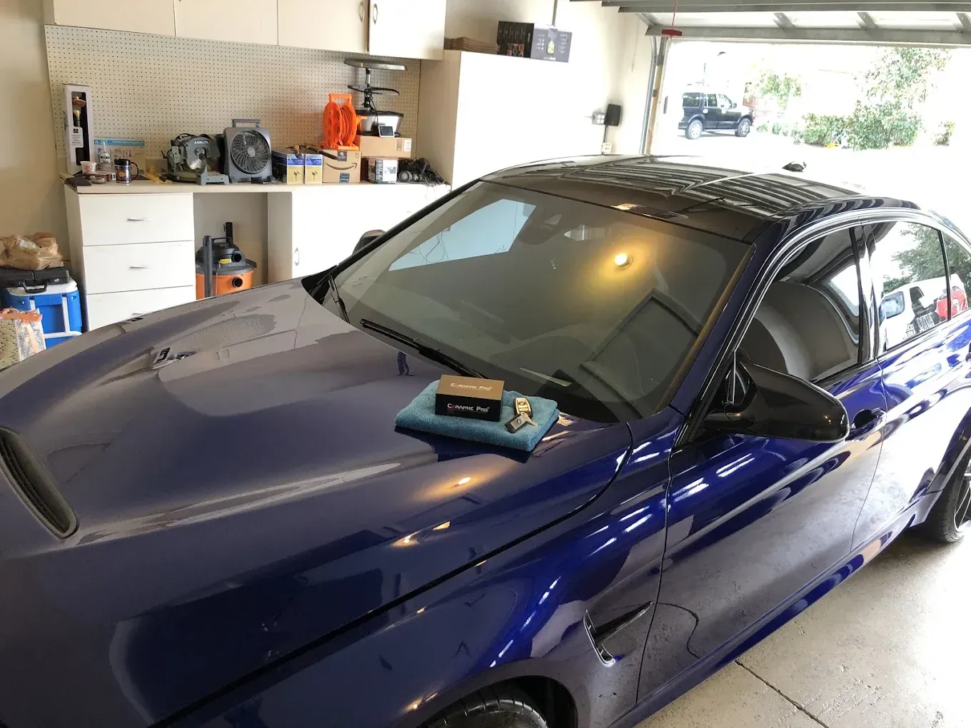 A blue BMW sports car in a garage. Black roof and side mirrors, a cleaning cloth on the hood.