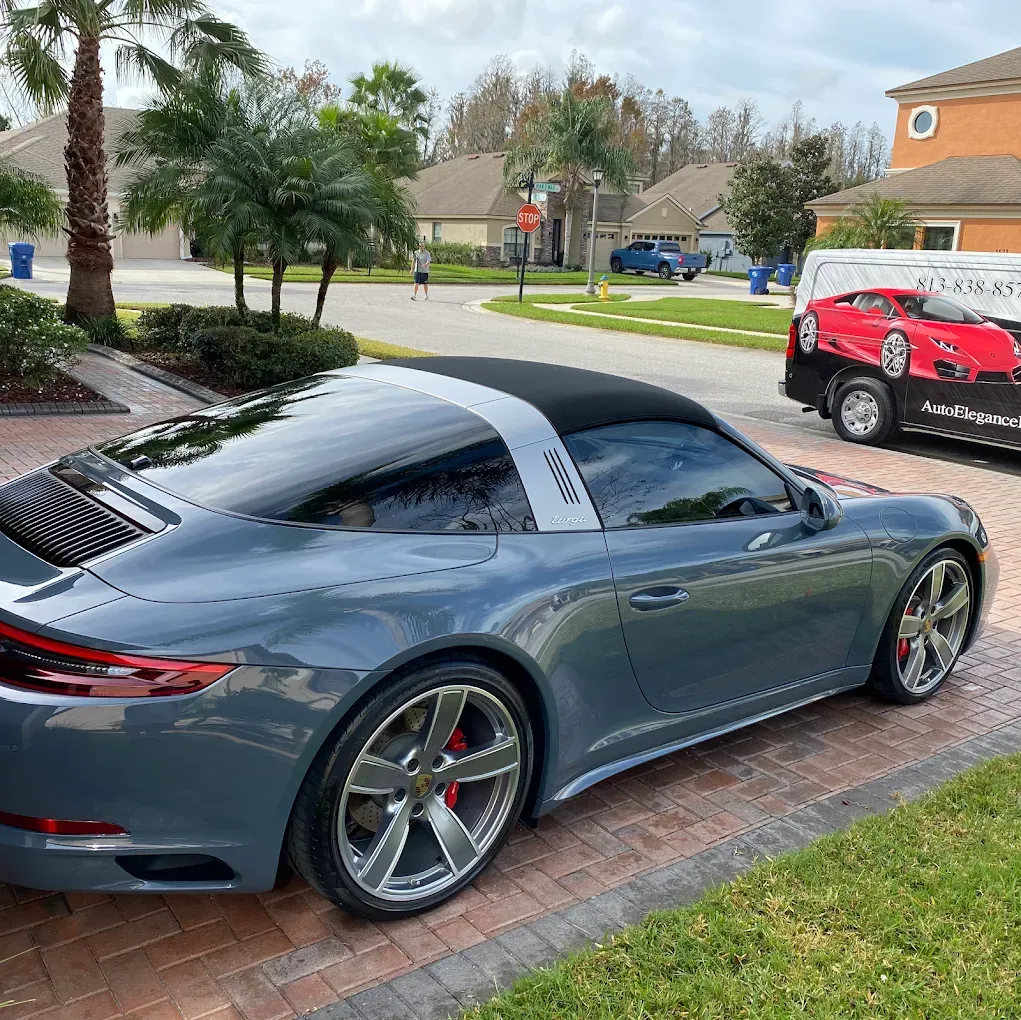 Gray Porsche Targa parked on a driveway with a black top and a trailer with a red car on it.