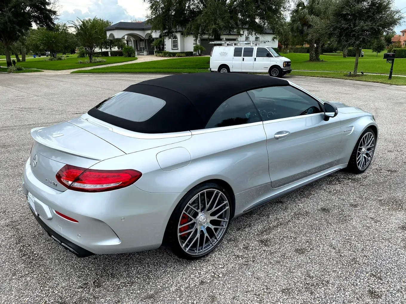 Silver Mercedes convertible with black top parked on gravel driveway.