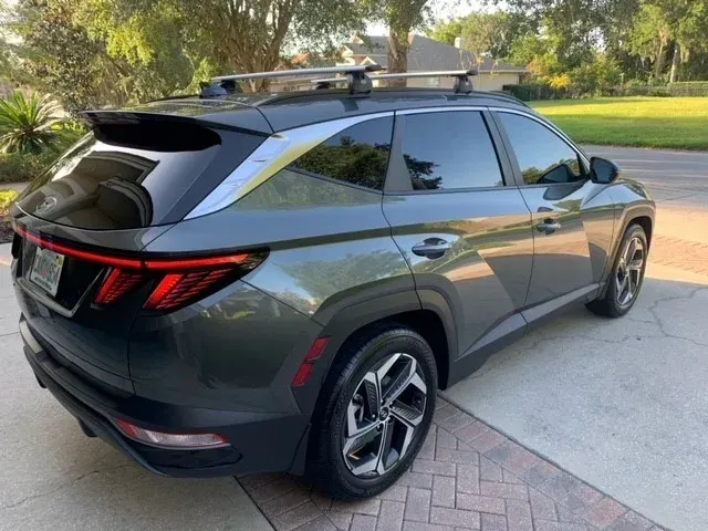 Dark gray Hyundai Tucson SUV with roof rack parked on a paved driveway.