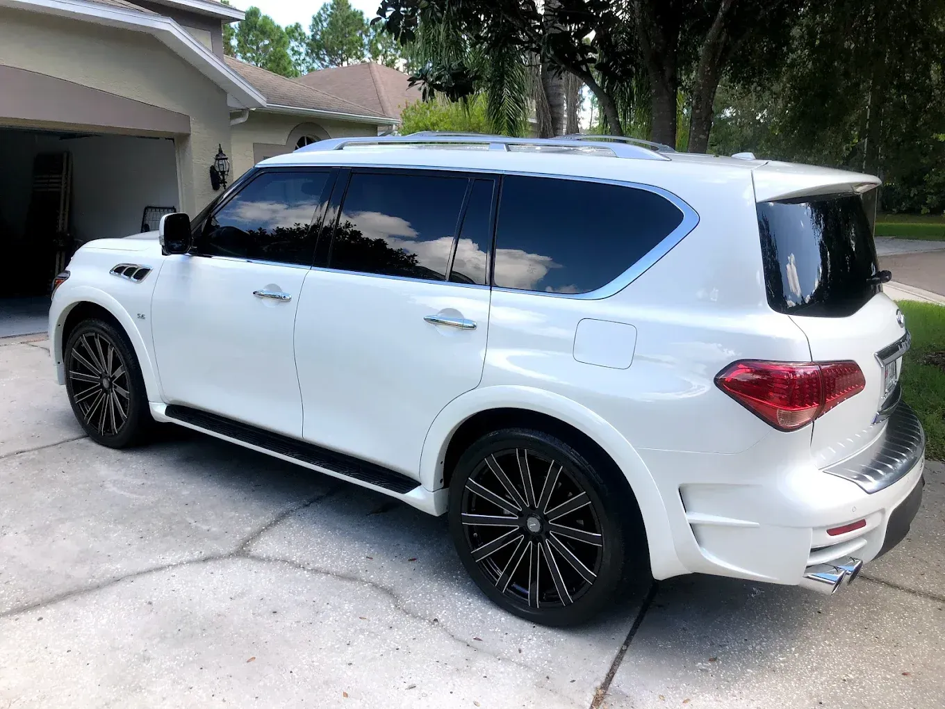 White Infiniti QX80 SUV with tinted windows and black rims parked in a driveway.