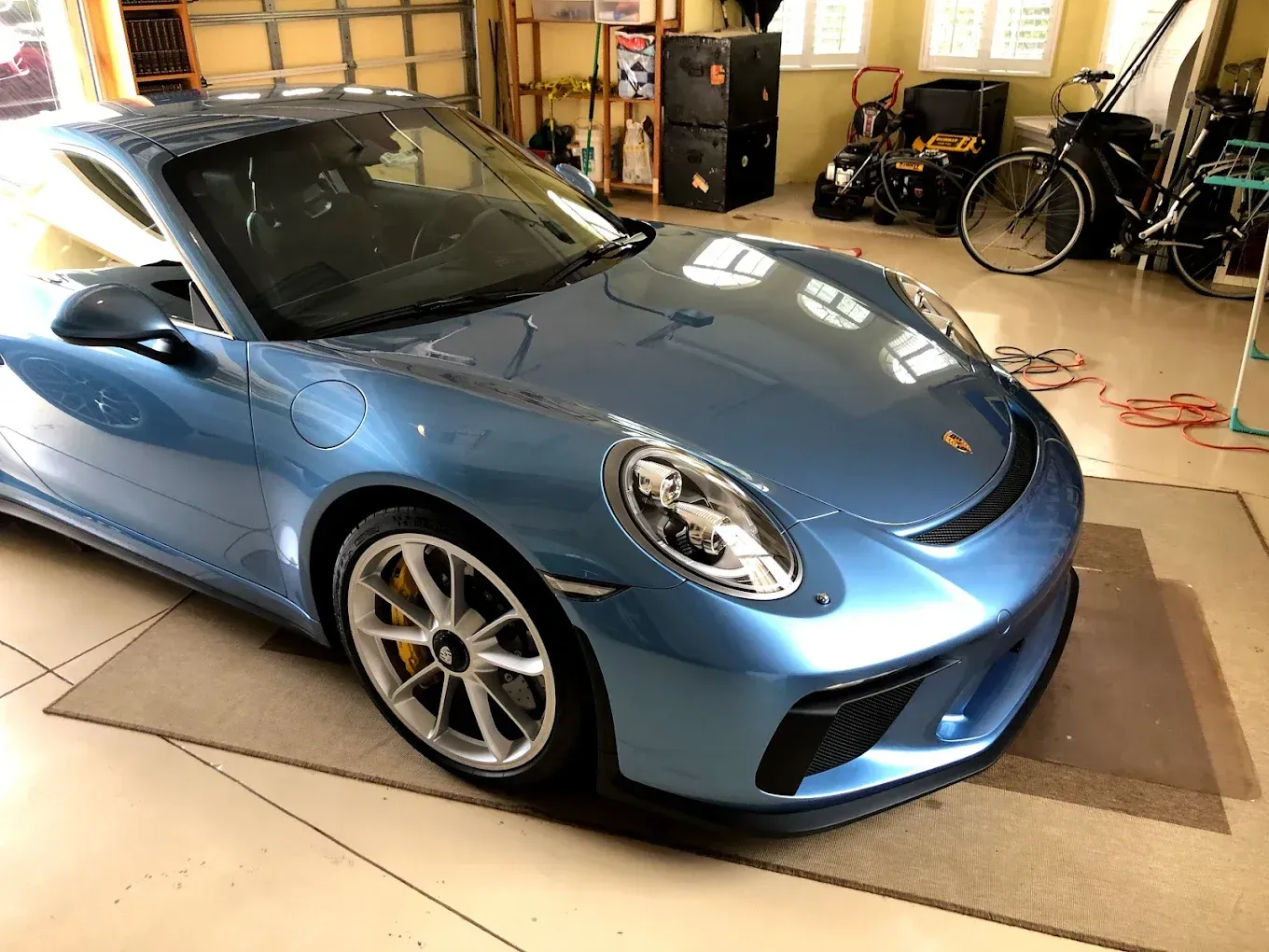 Blue Porsche sports car parked in a garage with garage door in the background.