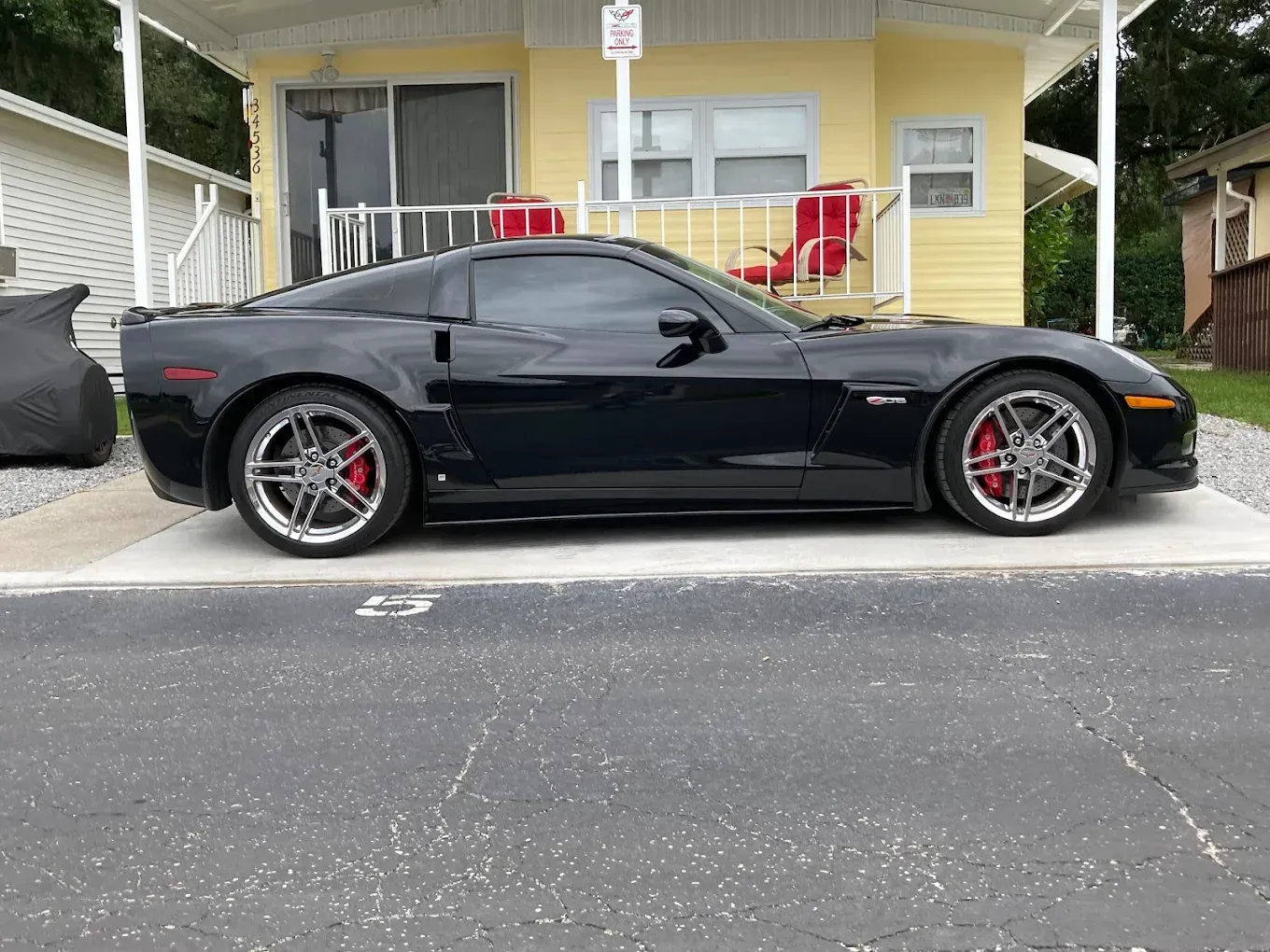 Black Corvette parked in front of a yellow mobile home, red brake calipers visible on the wheels.