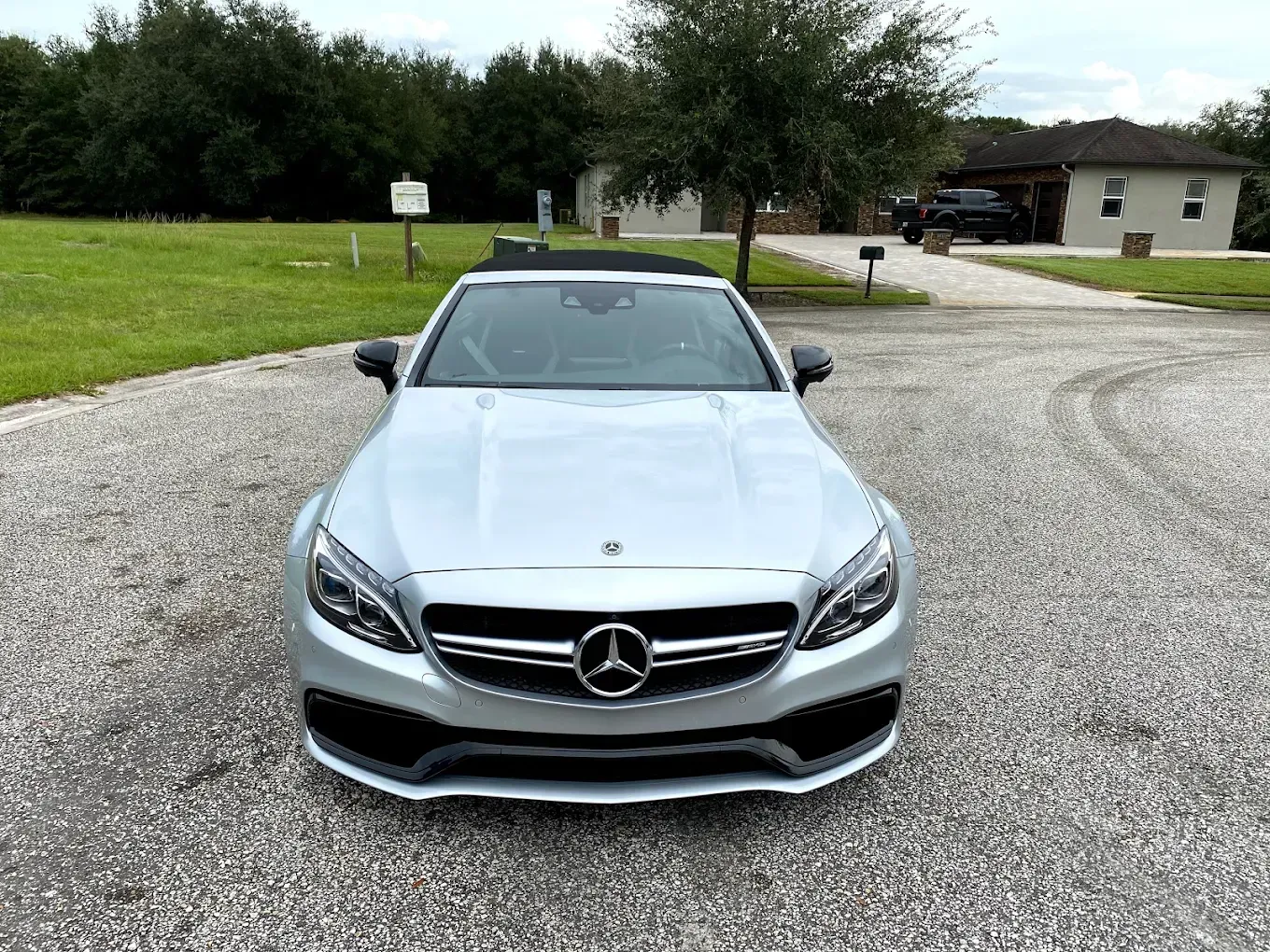 Silver Mercedes convertible parked on a gravel driveway, front view, with a house in the background.