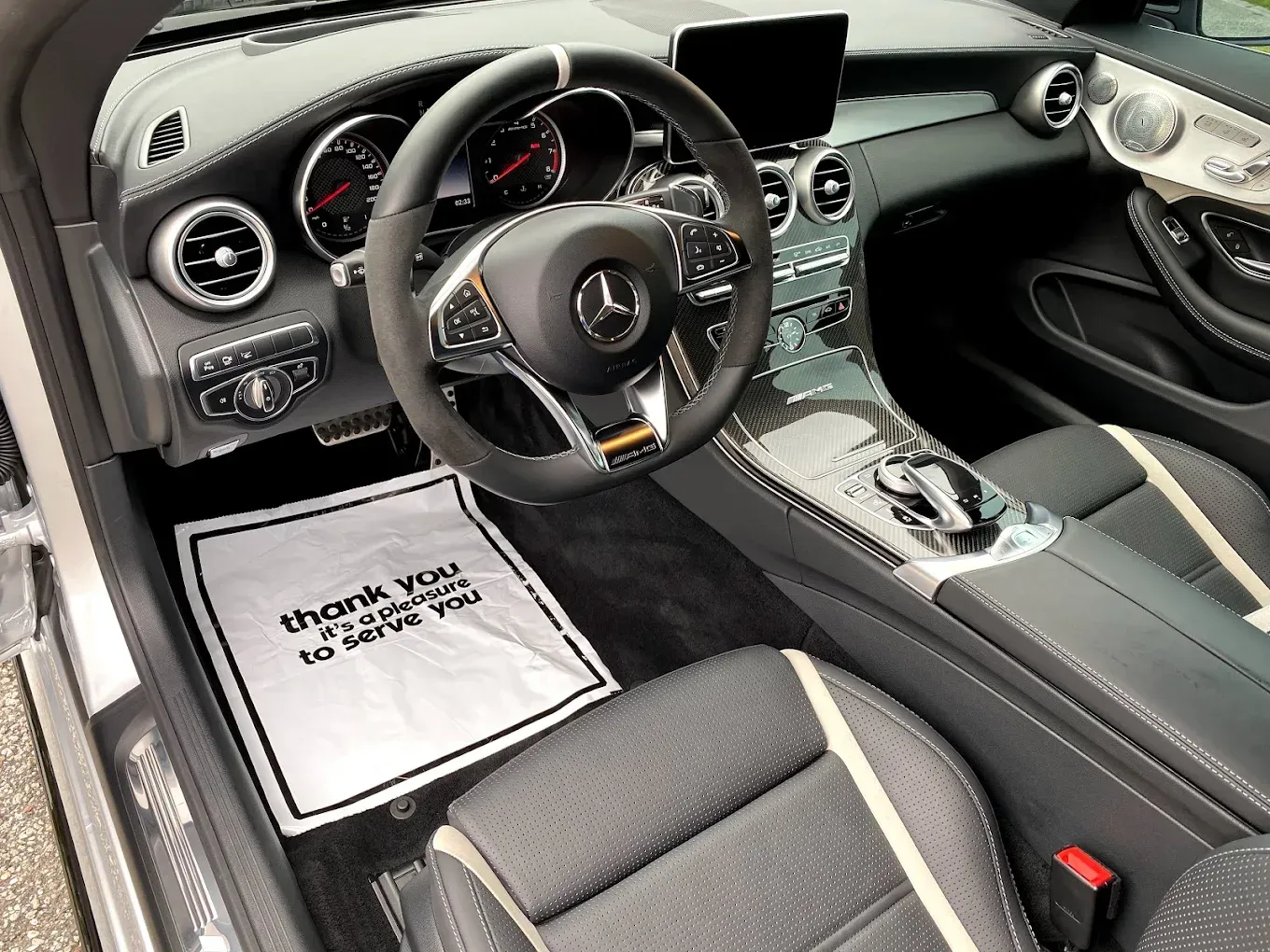 Interior of a black Mercedes-Benz car with a "thank you" floor mat.