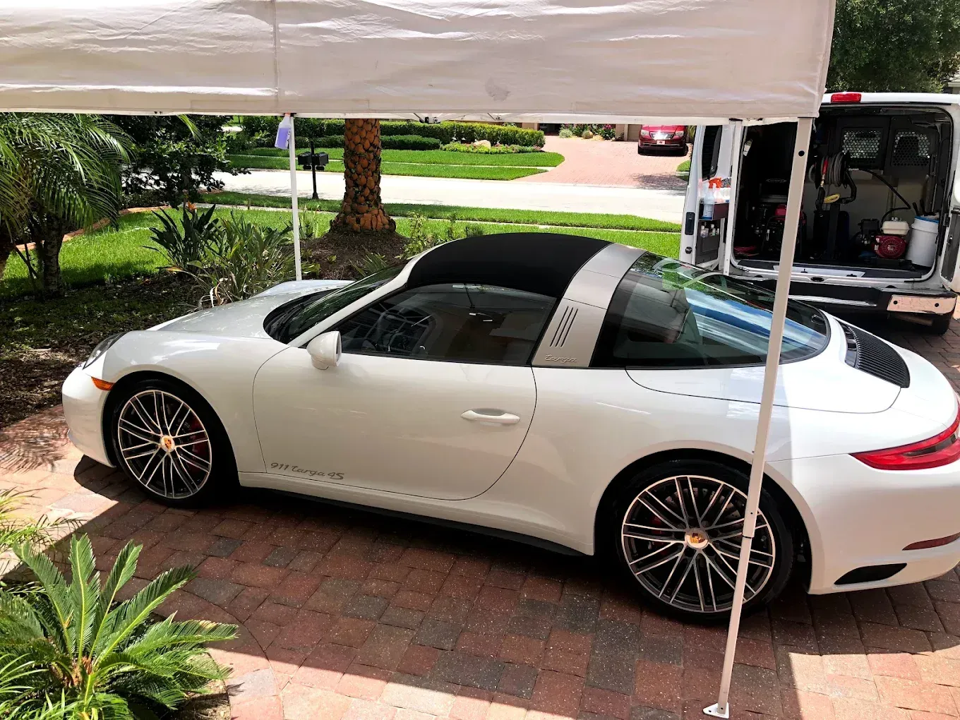 White Porsche Targa under a white canopy on a brick driveway, with a van in the background.