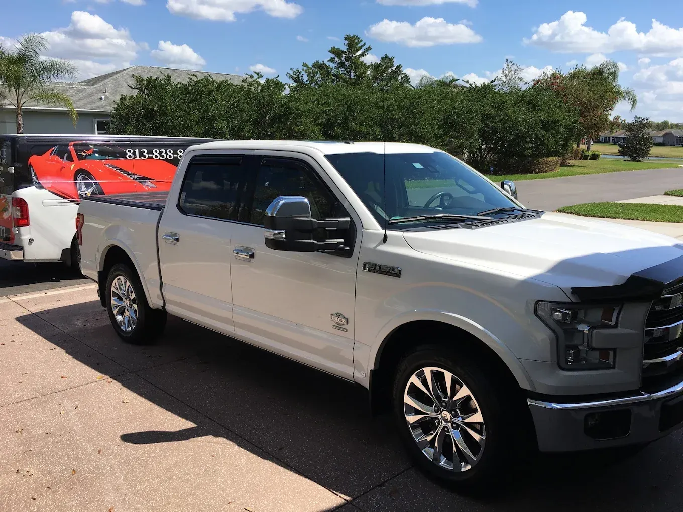 White Ford F-150 truck parked outside, chrome wheels, black hood protector. A car is visible in the background.