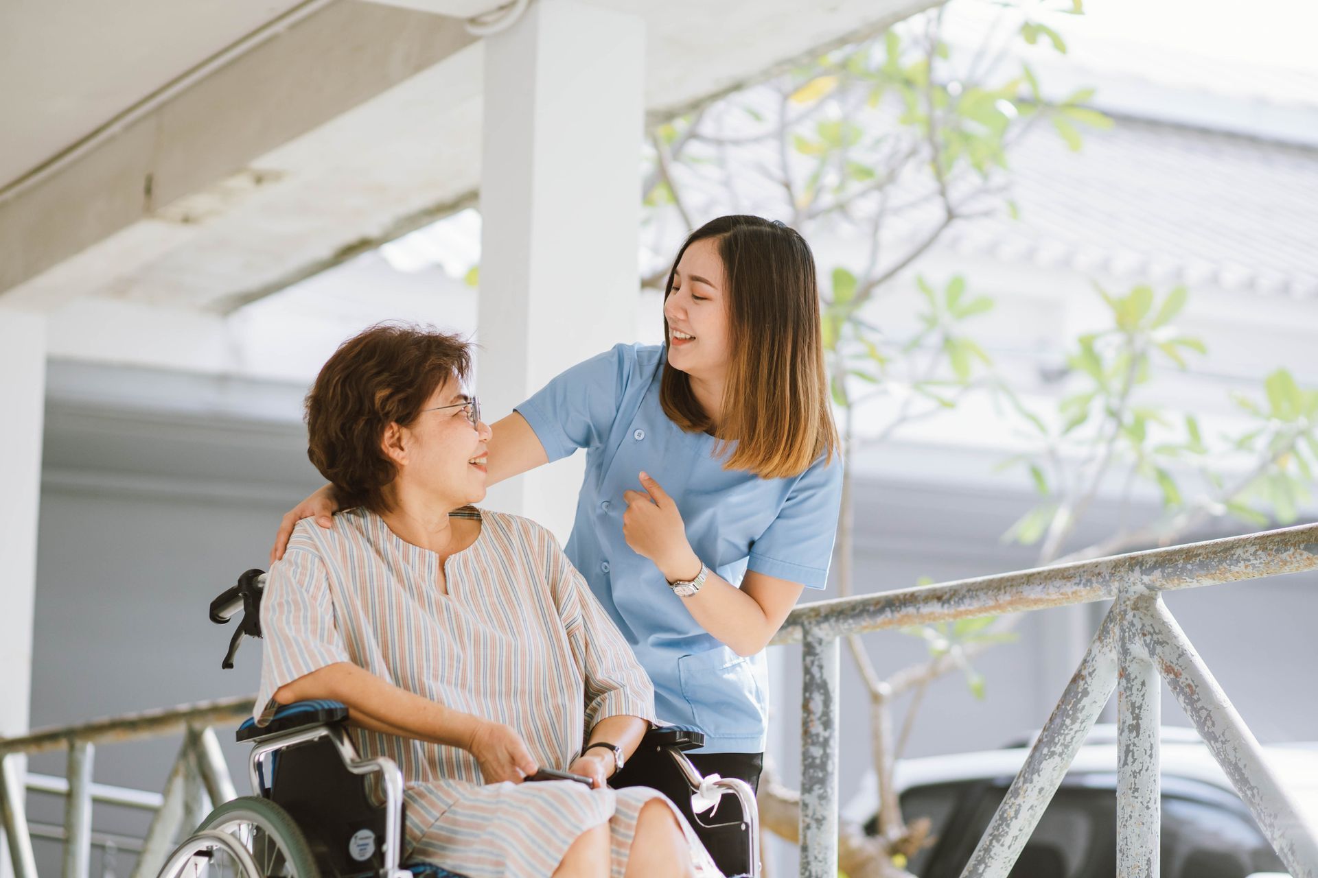 A healthcare worker helping a wheelchair user outdoors.