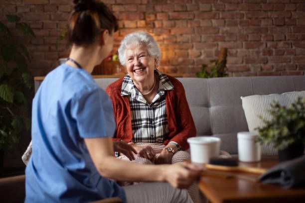 A smiling elderly woman chatting with a caregiver in a cozy living room.