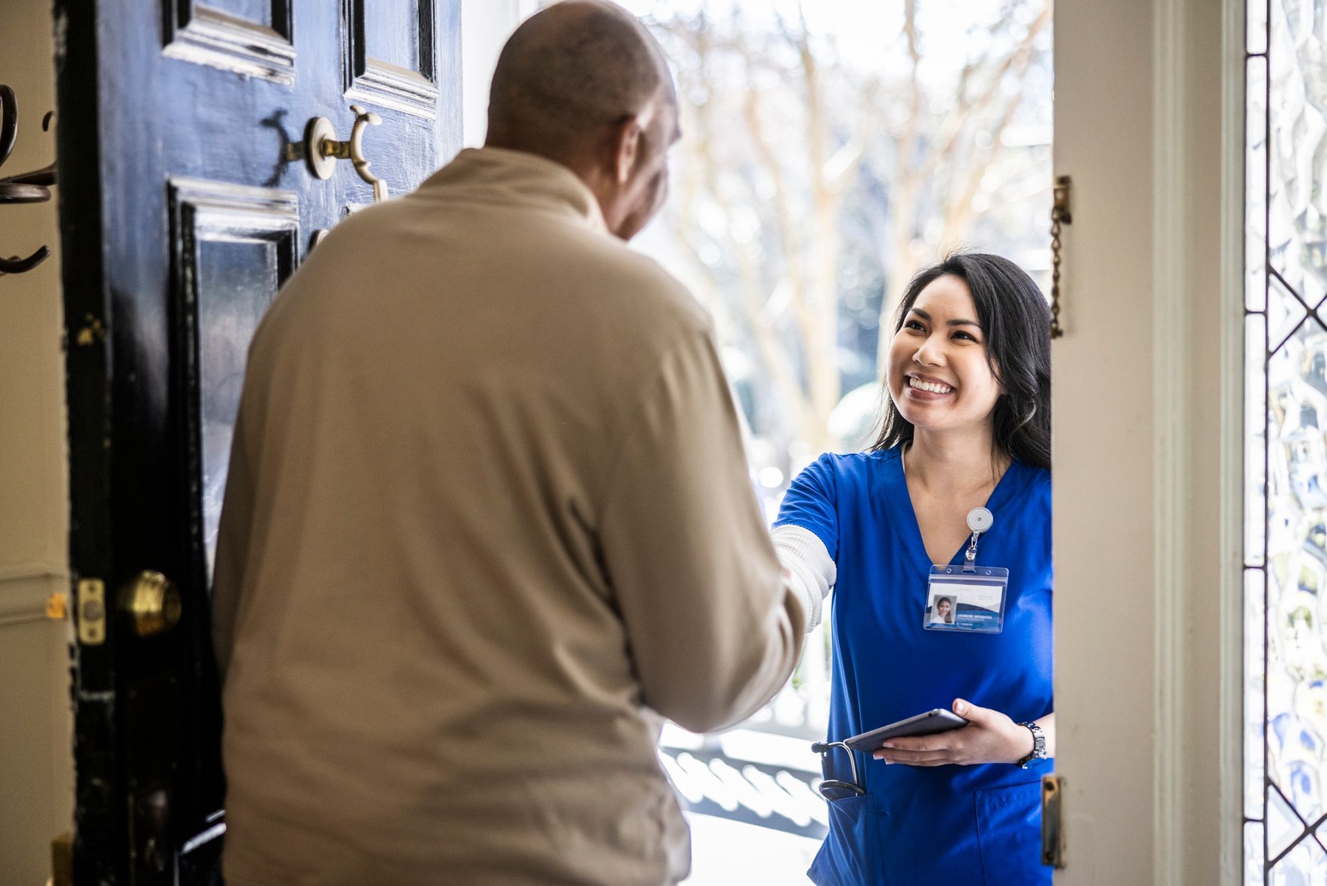 Senior man greeting home nurse at front door of home.