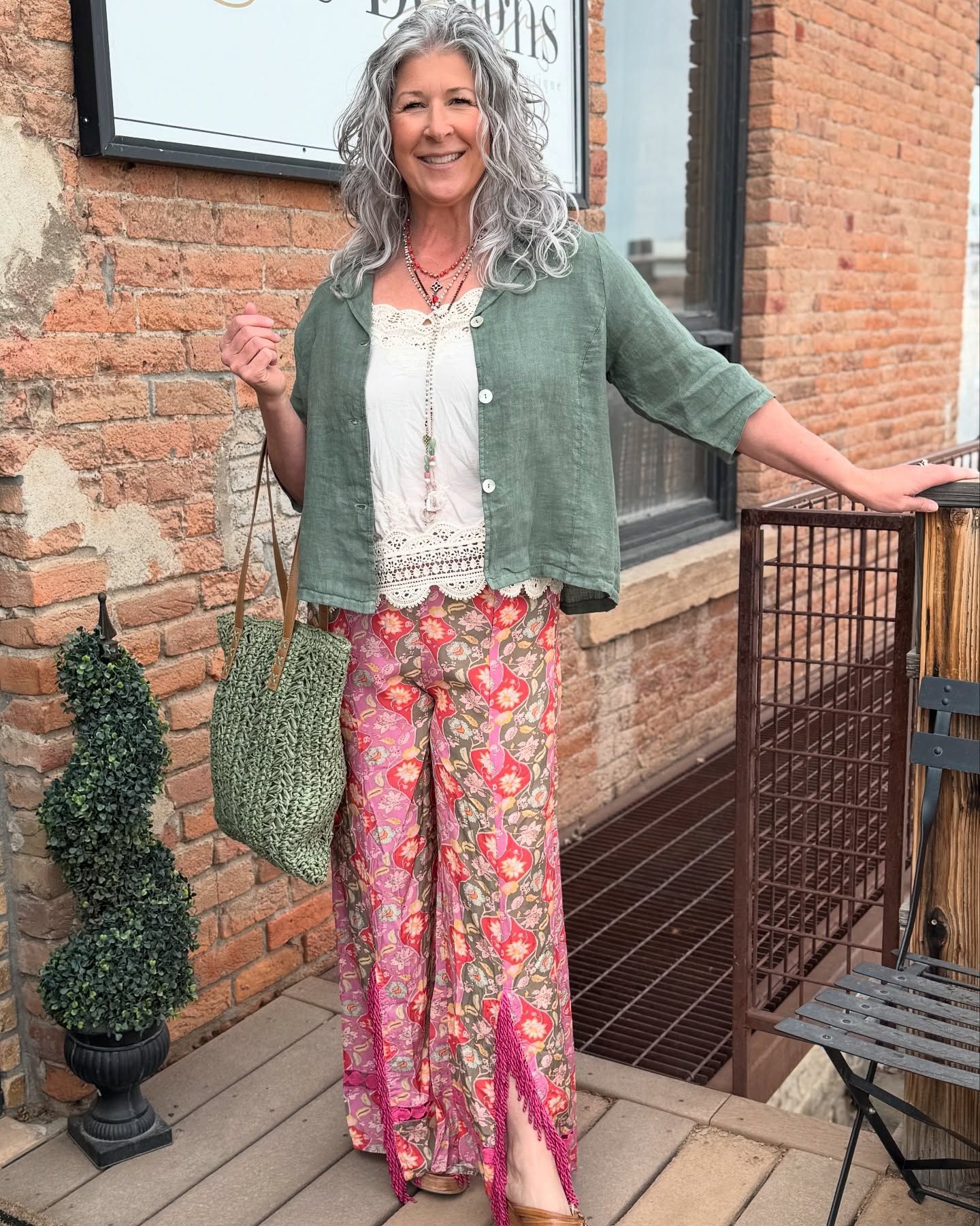 Woman in colorful floral pants, green cardigan, and crochet top, smiling outdoors.