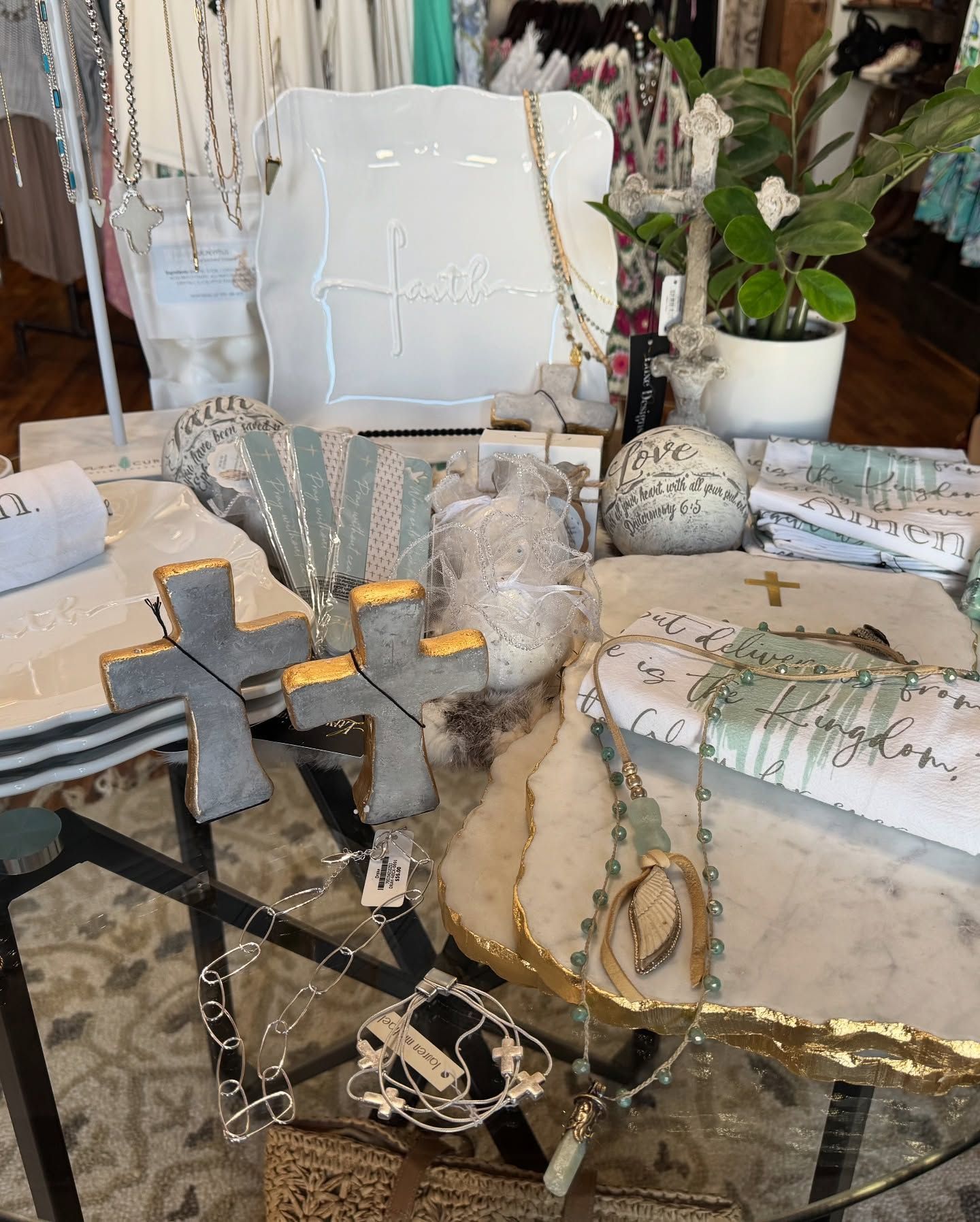 Display of home decor items, including crosses, towels, and jewelry, on a glass-topped table.