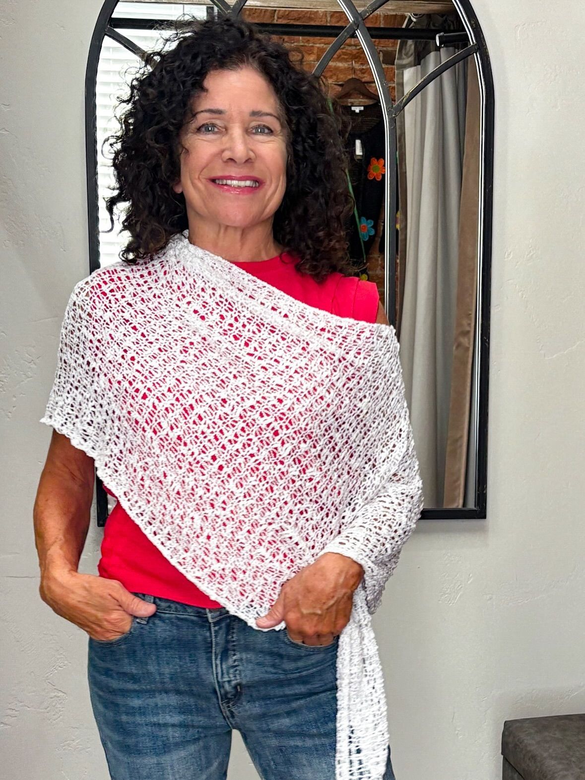 Woman in red shirt and jeans wearing a white shawl, smiling indoors.