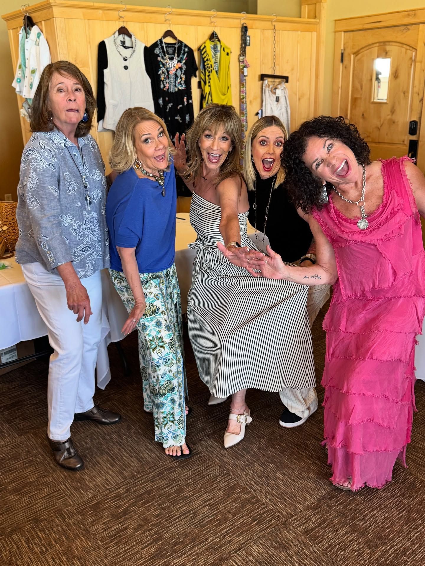 Group of women posing playfully in front of clothing display; one in zebra print dress.