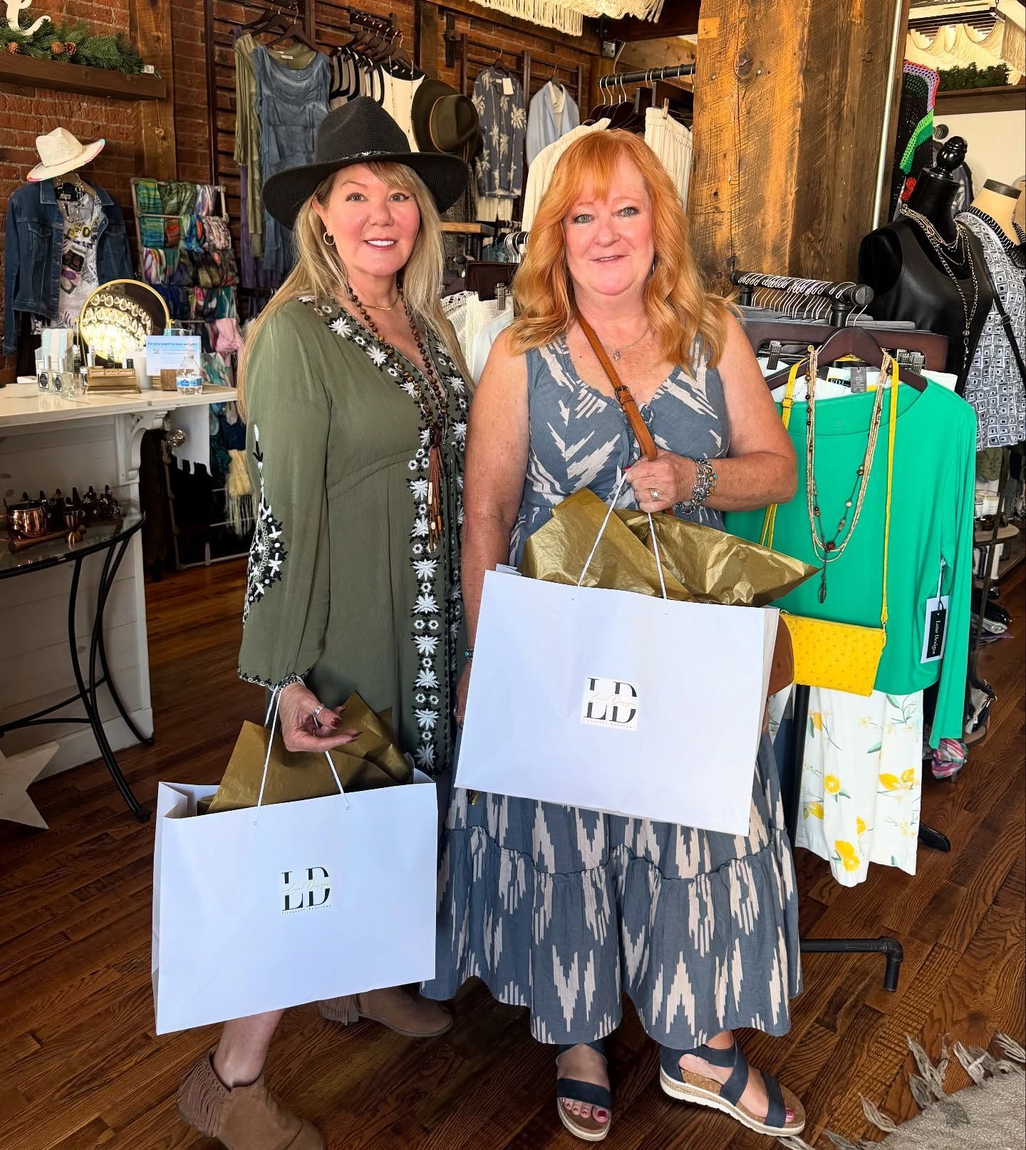Two women holding shopping bags pose inside a clothing boutique.