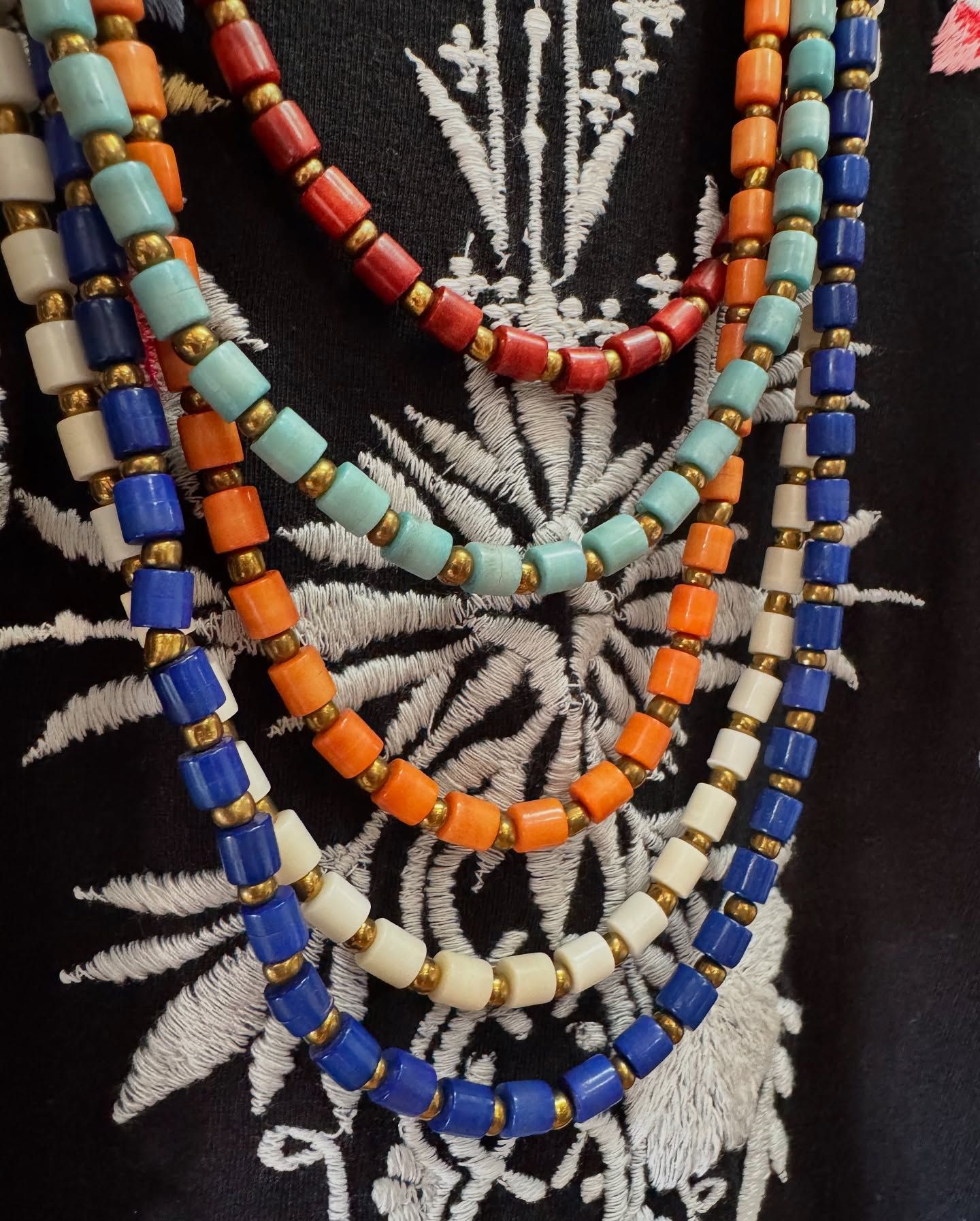 Colorful beaded necklaces layered over a black and white embroidered garment.