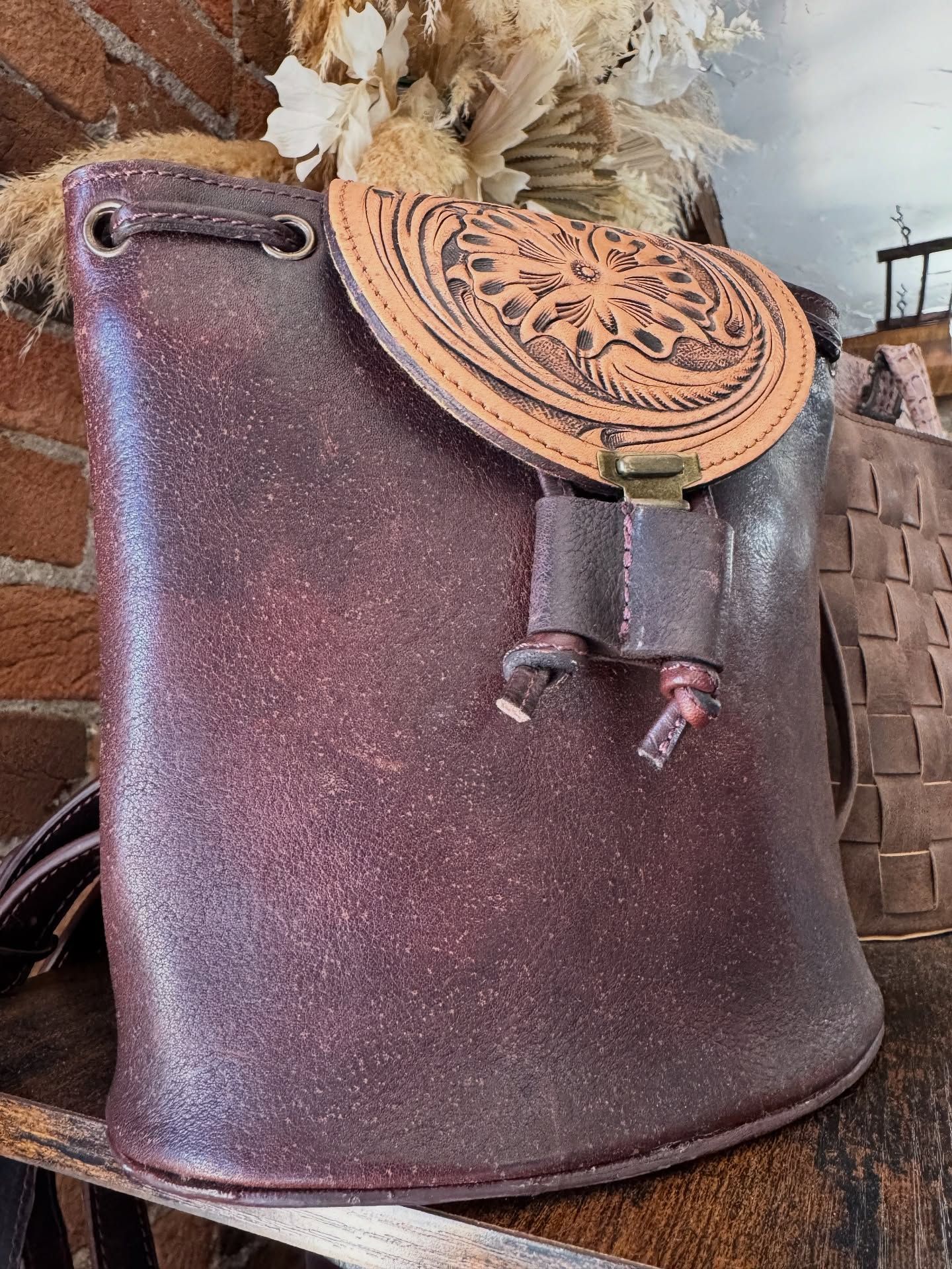 Burgundy leather backpack with tan, embossed flap. Drawstring closure and decorative strap detail.