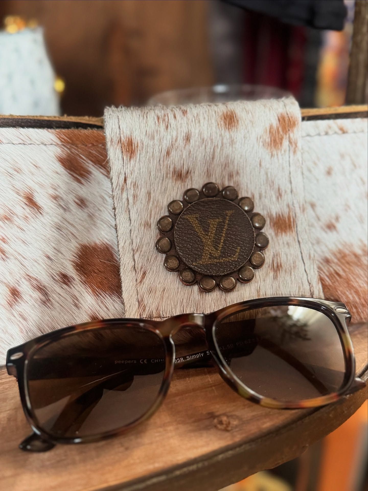 Sunglasses resting on a cowhide wallet with a Louis Vuitton medallion.