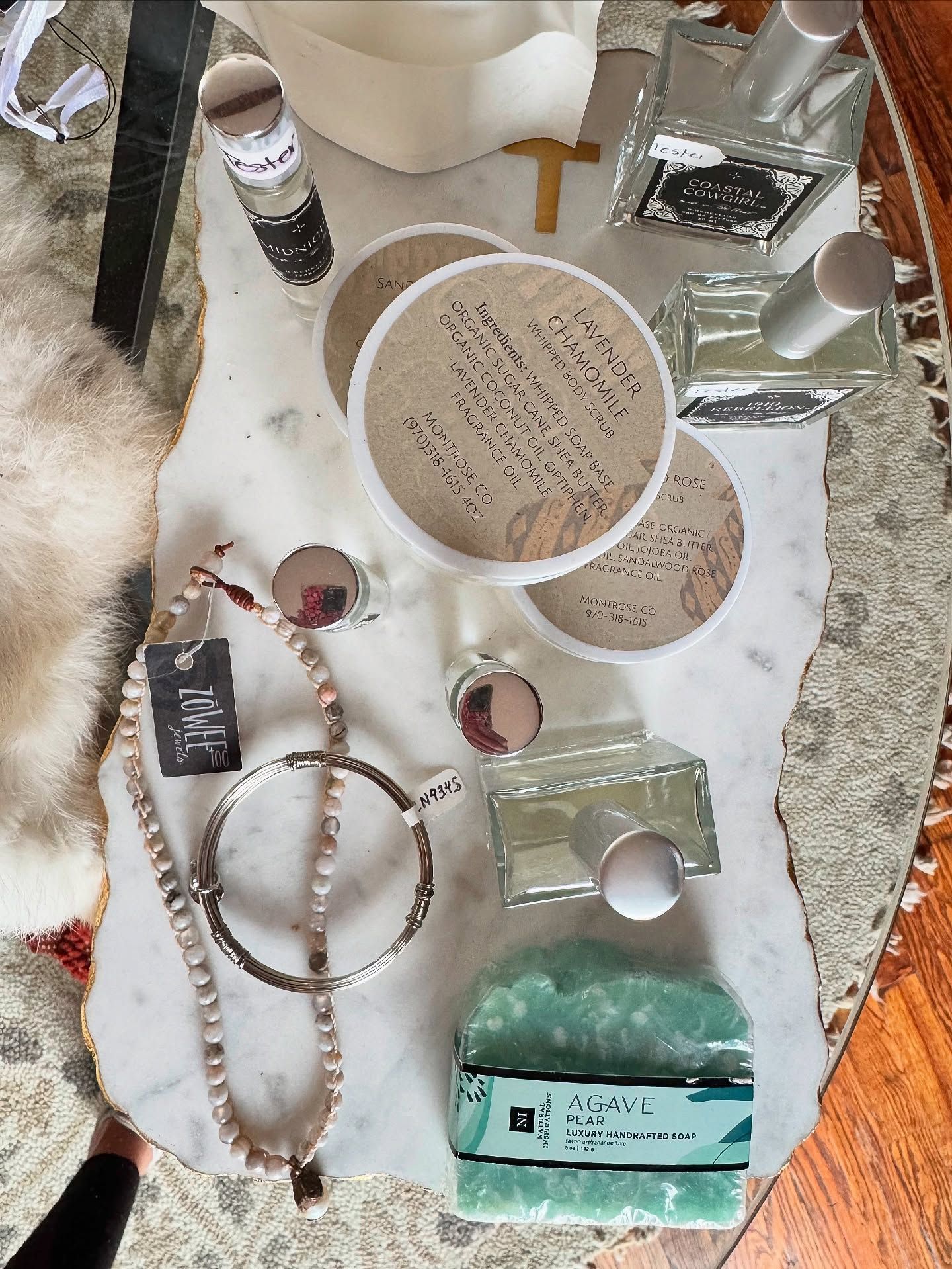A flat lay of beauty products, jewelry, and a cross on a marble tray.