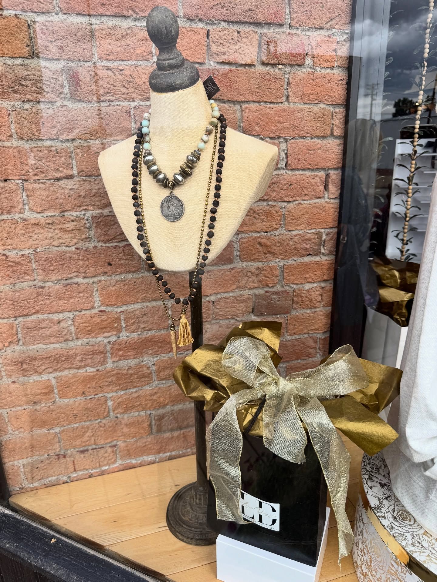 Mannequin wearing necklaces in a store window with a gift bag.