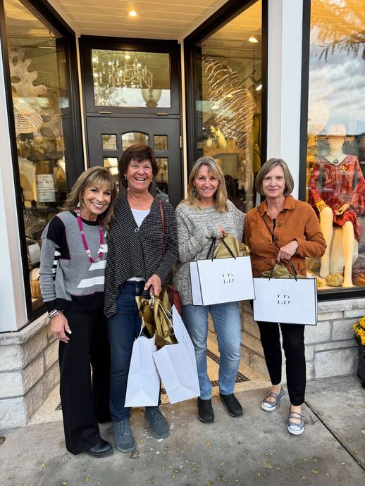 Four women holding shopping bags stand outside a store with glass windows.