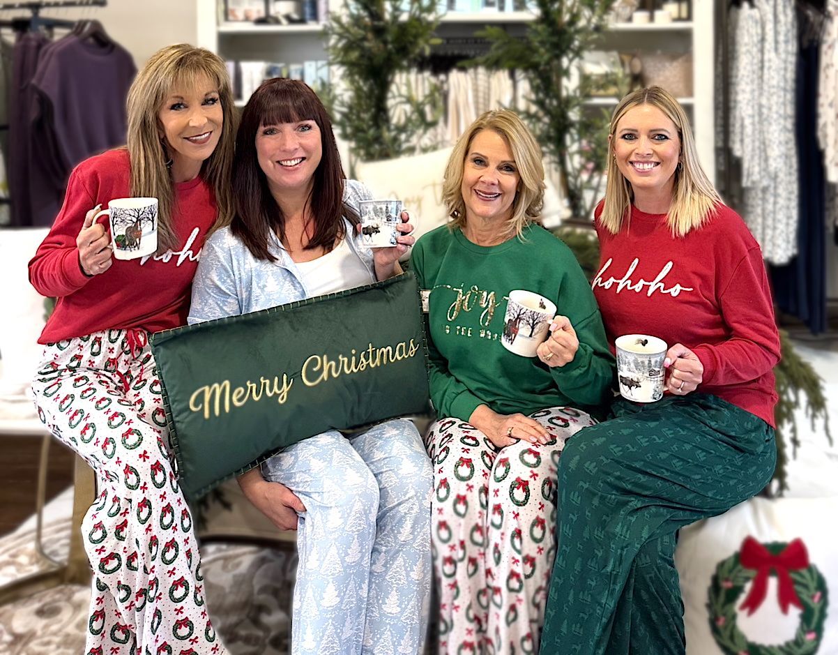 Four women in Christmas pajamas holding mugs and a pillow.