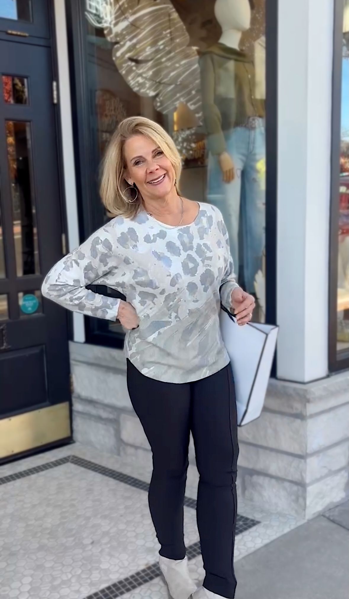 Woman in sequined top and black pants stands in front of a store window.