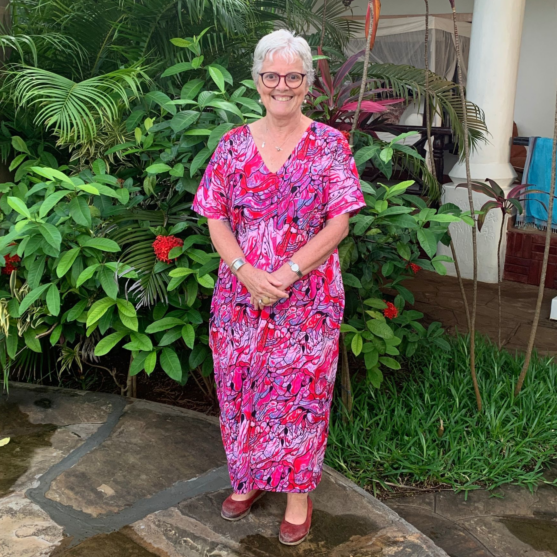 Person in a pink floral dress standing on stone steps in a lush garden.