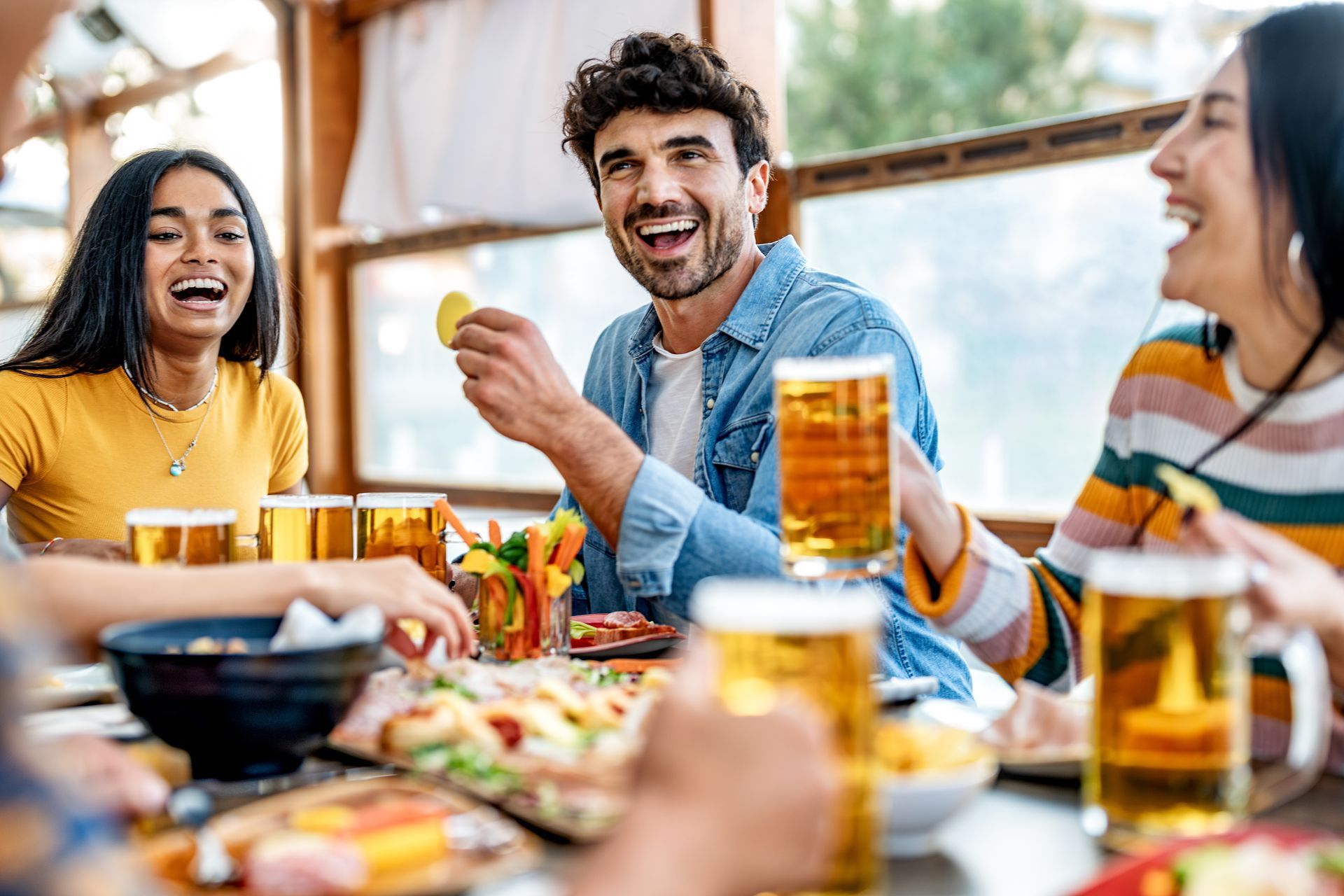 Group of diverse young adults enjoying food and drinks outdoors around a table