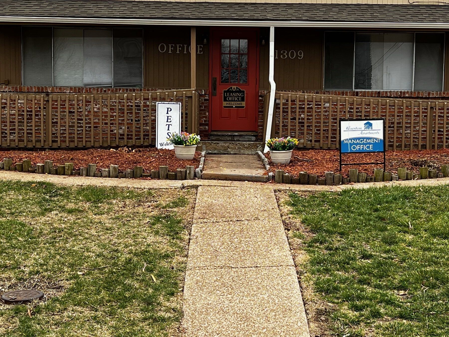 Brown building with red door, signs for "Office" and "Pets," and a sidewalk leading to the entrance.
