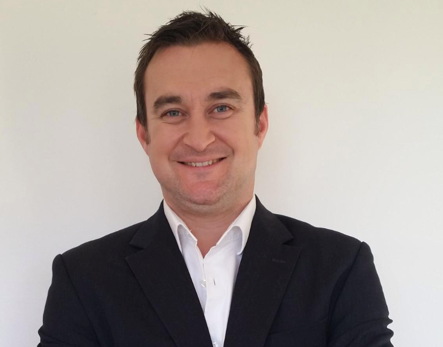 Man in a suit smiles at the camera, white background.