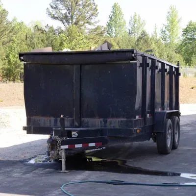 A green dumpster is parked next to an orange trailer