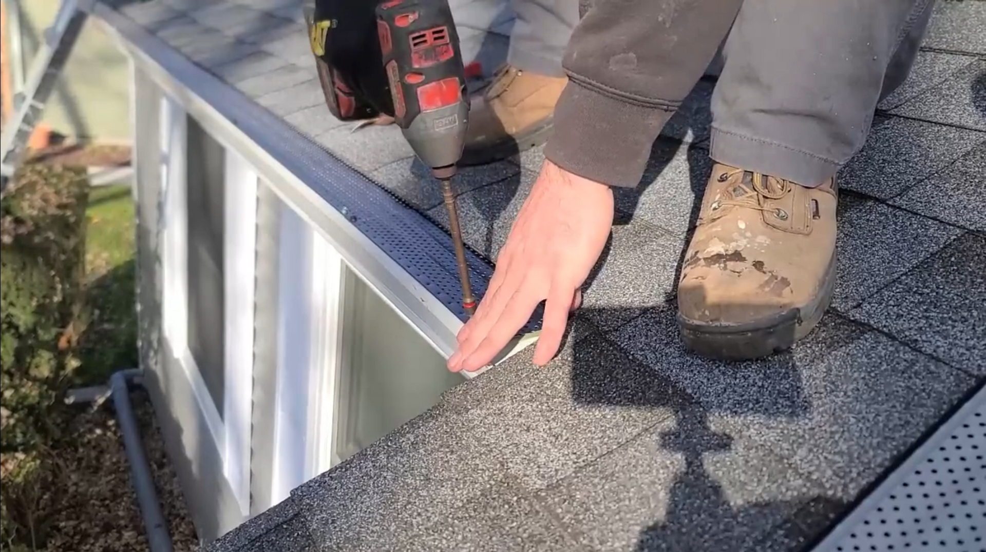 man on top of roof installing gutter guards with a drill