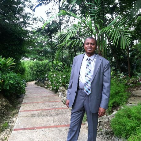 a man in a suit and tie stands in a garden, Walline Williams, owner of Baje Cafe & Catering, LLC