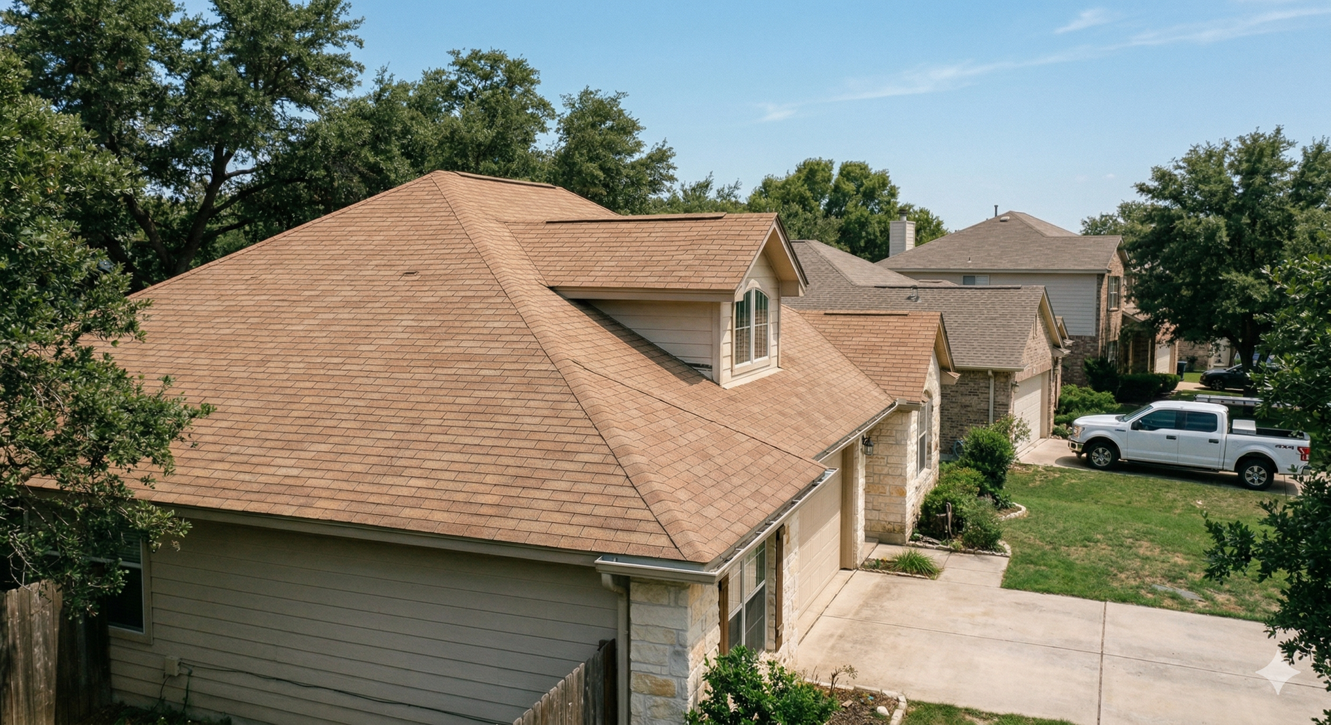 Aerial view of a suburban house with a tan shingled roof, light brick exterior, and a white pickup truck in the driveway.
