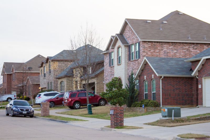 a row of houses in a residential neighborhood with cars parked in front of them The Amish Roofer.