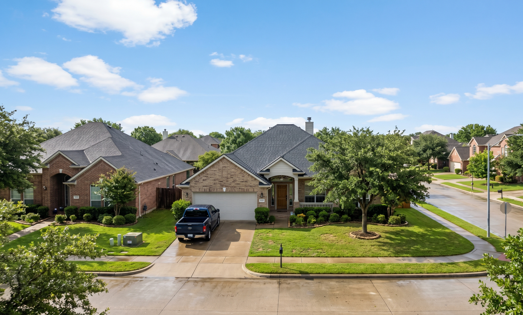 Suburban brick homes with a parked black SUV and a tree-lined street on a sunny day