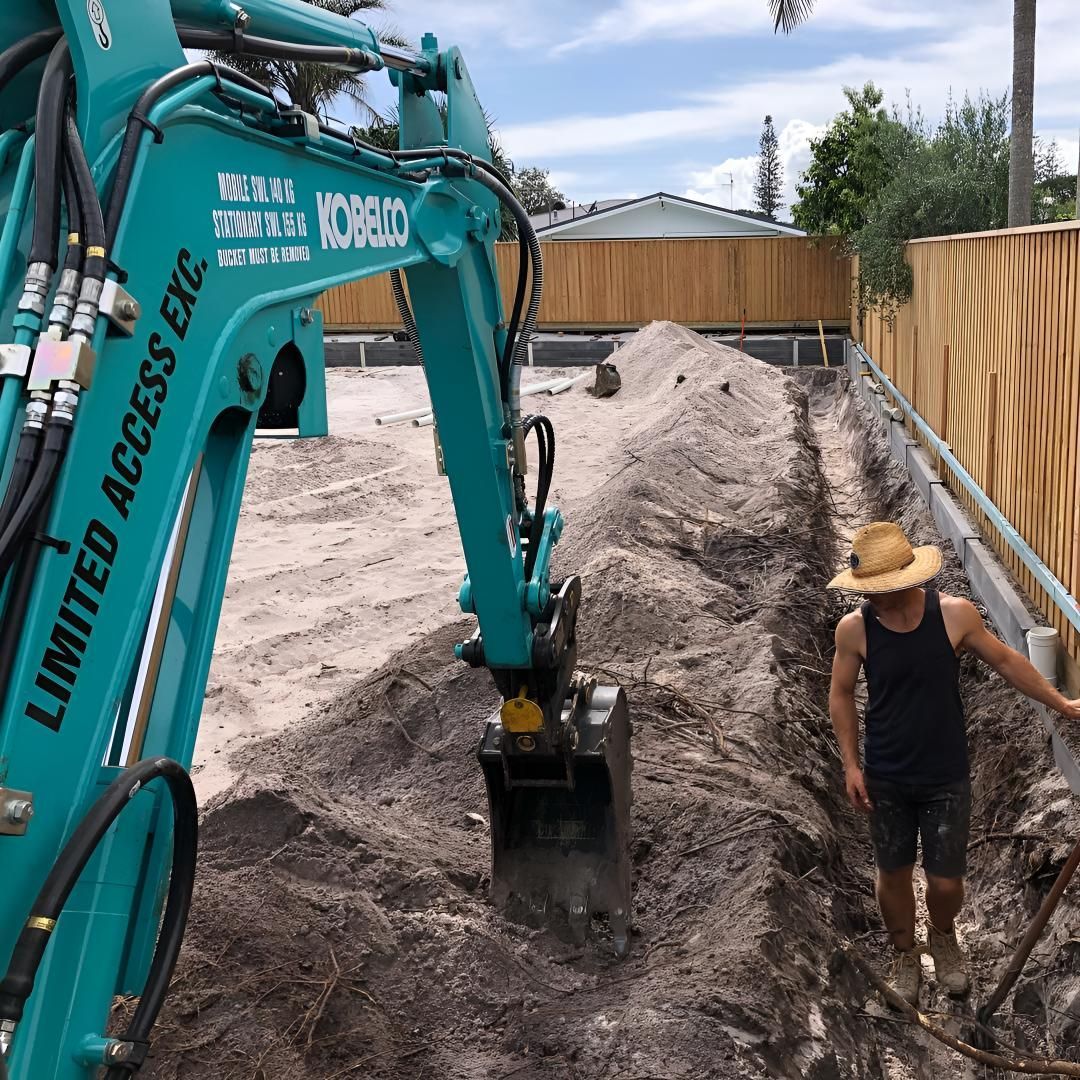A Man in a Hat is Digging in the Dirt in Front of a Limited Access Excavator — Limited Access Excavation In Pottsville, NSW