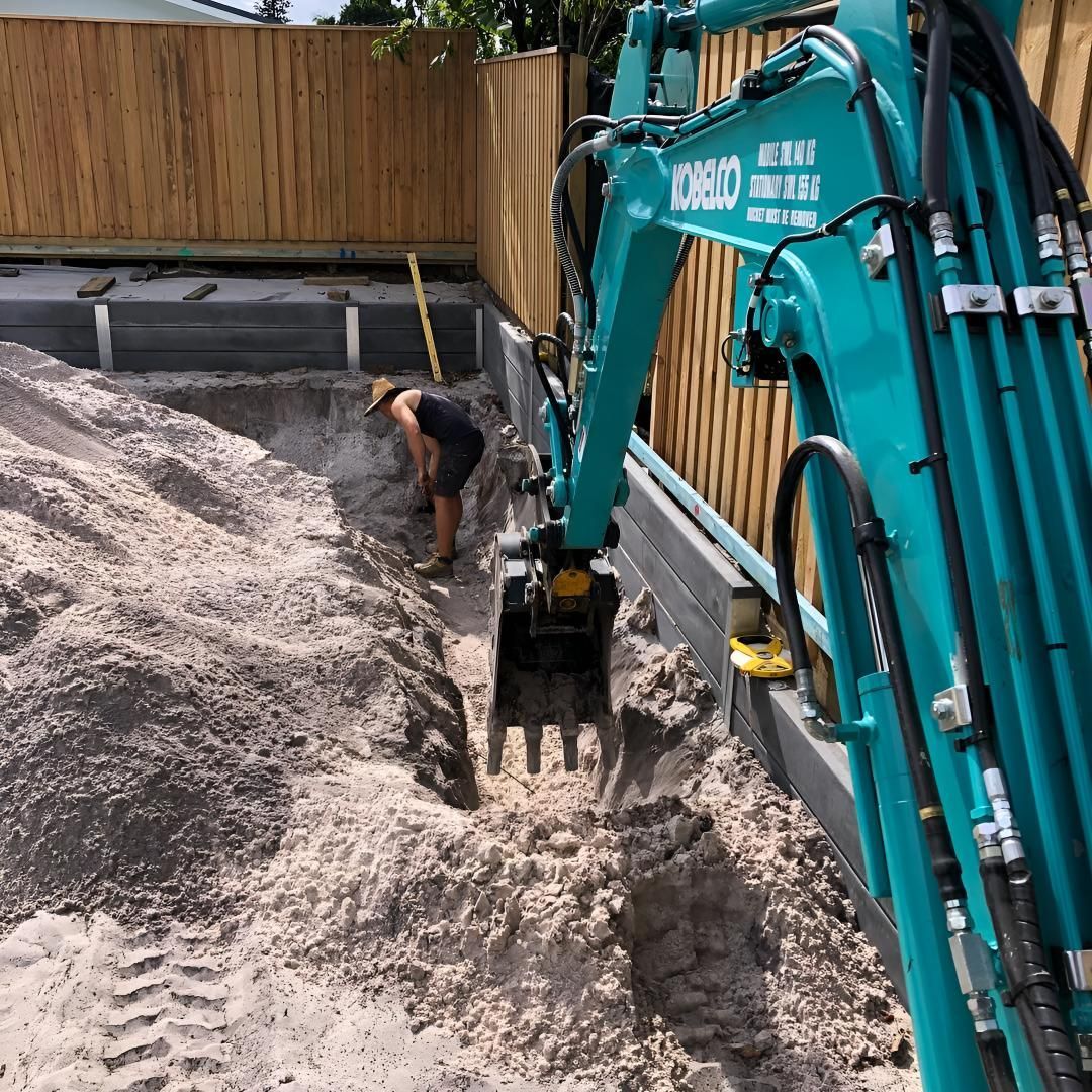 A Man is Digging a Hole in the Ground Next to a Blue Excavator — Limited Access Excavation In Mullumbimby, NSW