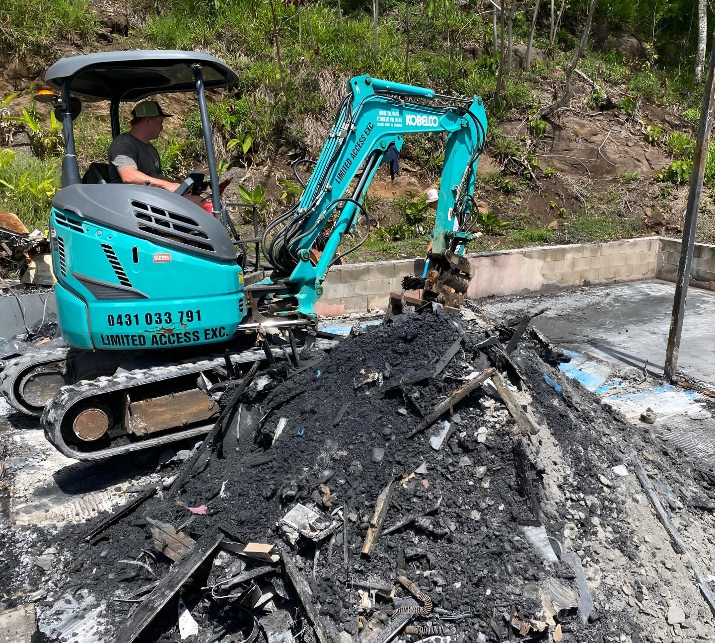A Man is Driving a Small Excavator Next to a Pile of Rubble — Limited Access Excavation In Yamba, NSW