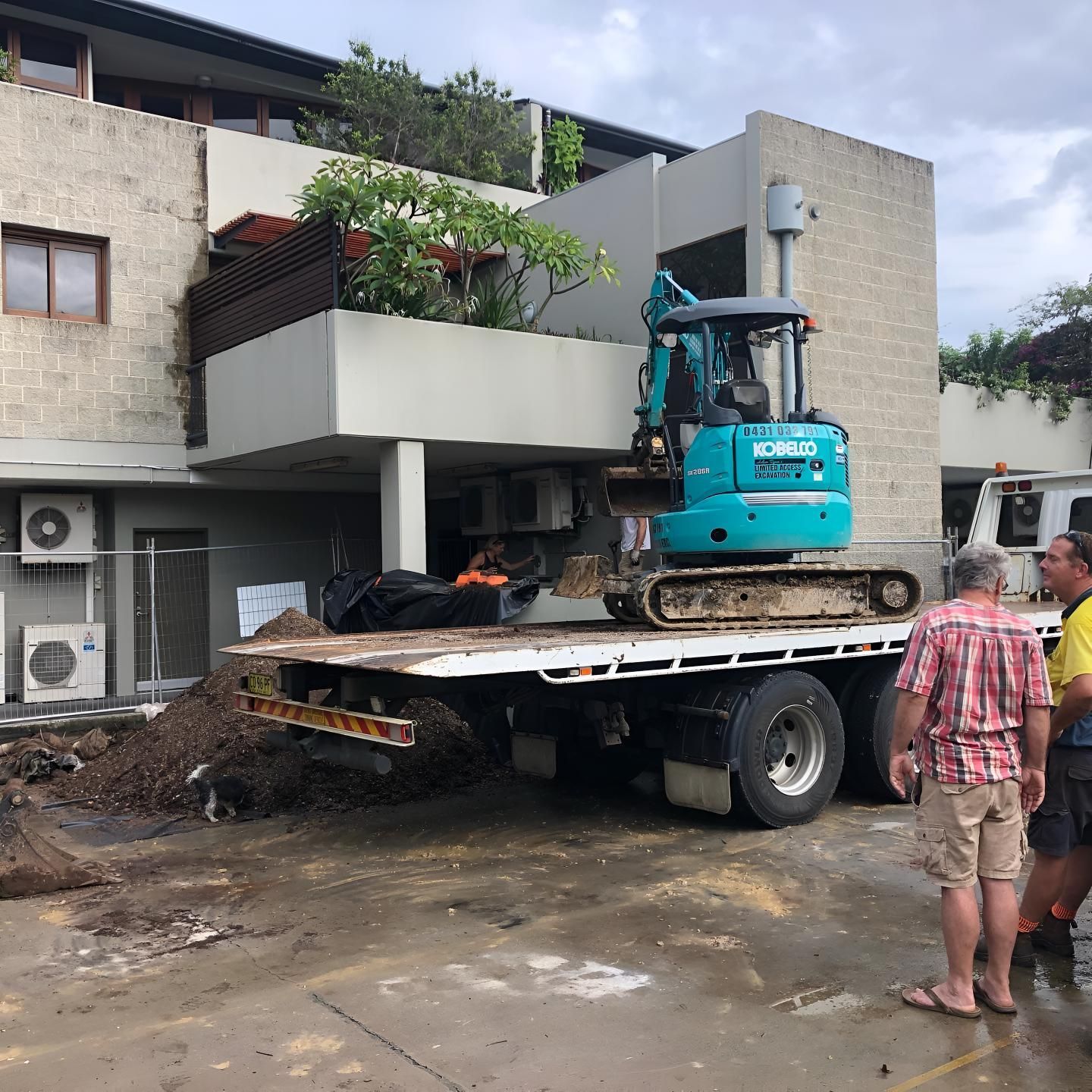 A Blue Excavator is on a Flatbed Truck in Front of a Building — Limited Access Excavation In Grafton, NSW