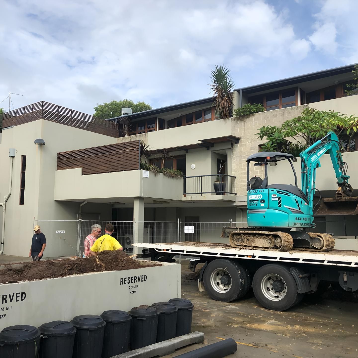 A Blue Excavator is on a Flatbed Truck in Front of a Building — Limited Access Excavation In Ballina, NSW
