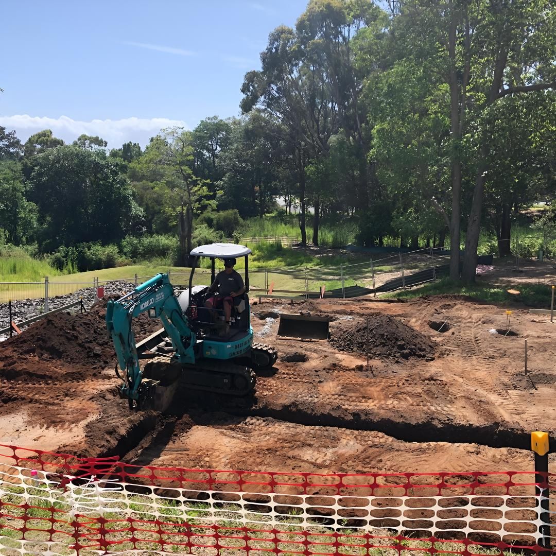 A Man is Driving a Small Excavator in a Dirt Field — Limited Access Excavation In Yamba, NSW