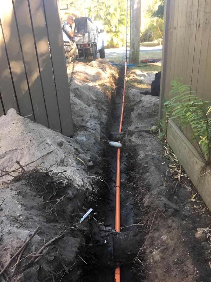 A Man is Working on a Pipe in the Dirt Next to a Fence — Limited Access Excavation In Suffolk Park, NSW