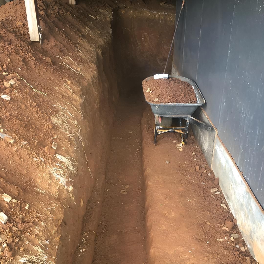 A Wheelbarrow Filled With Dirt is Sitting in a Trench Next to a Wall — Limited Access Excavation In Grafton, NSW